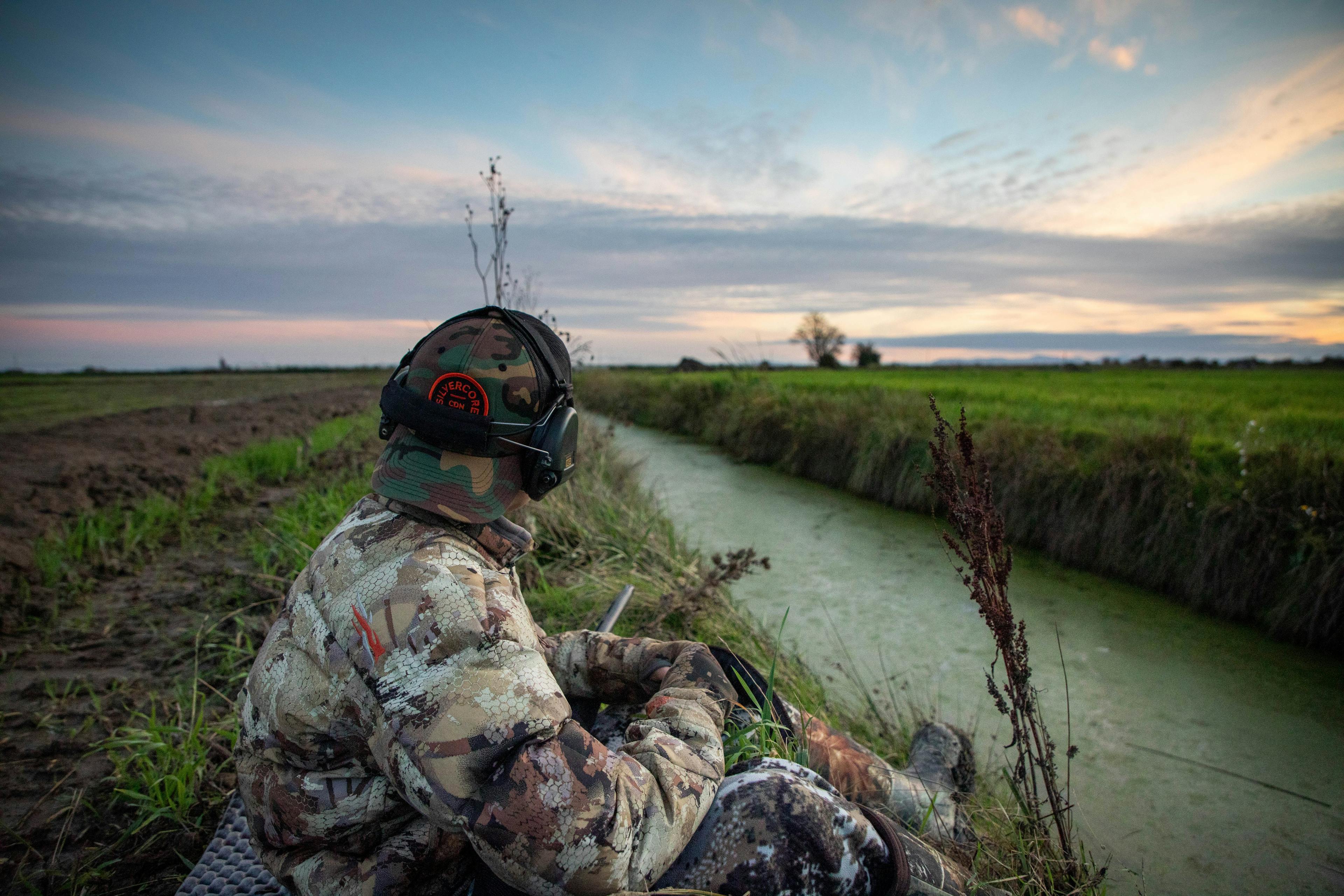 A person in hunting gear looking out across a field